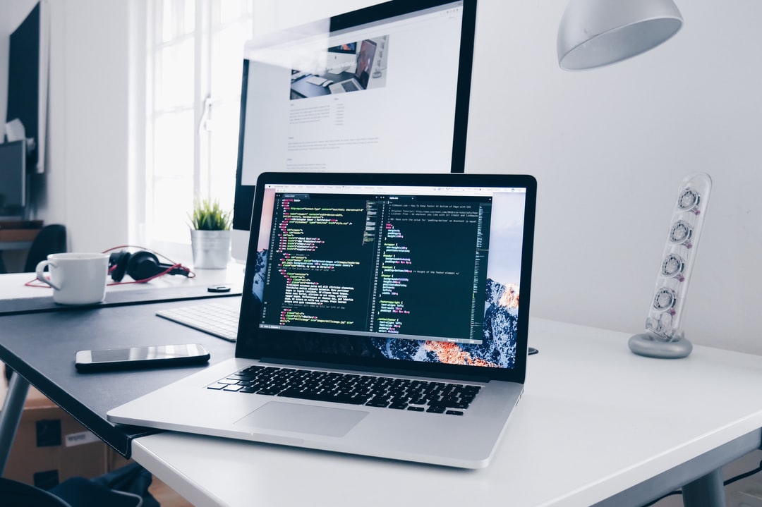 two computers on top of a desktop with the nearest laptop with code pulled up on the screen